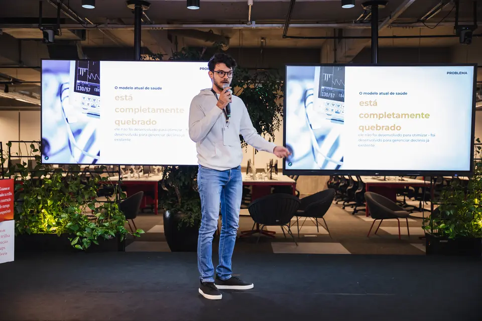 Speaker presenting on stage between two screens