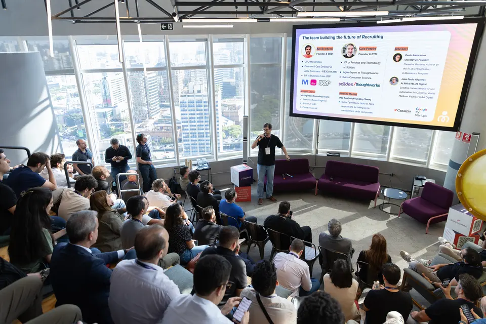 Audience watching a talk in a sunlit room above the city